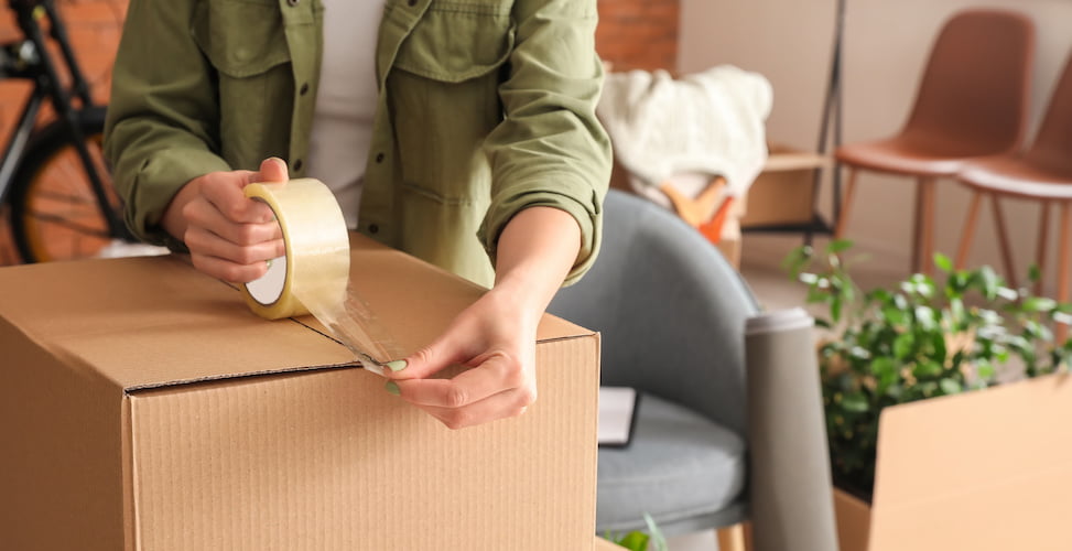 person taping cardboard box surrounded by packing items