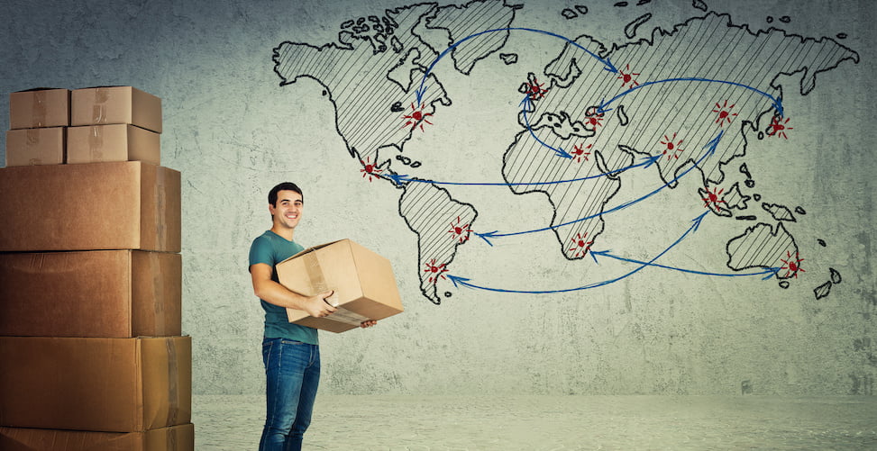 man in front of world map and stack of boxes holding cardboard box