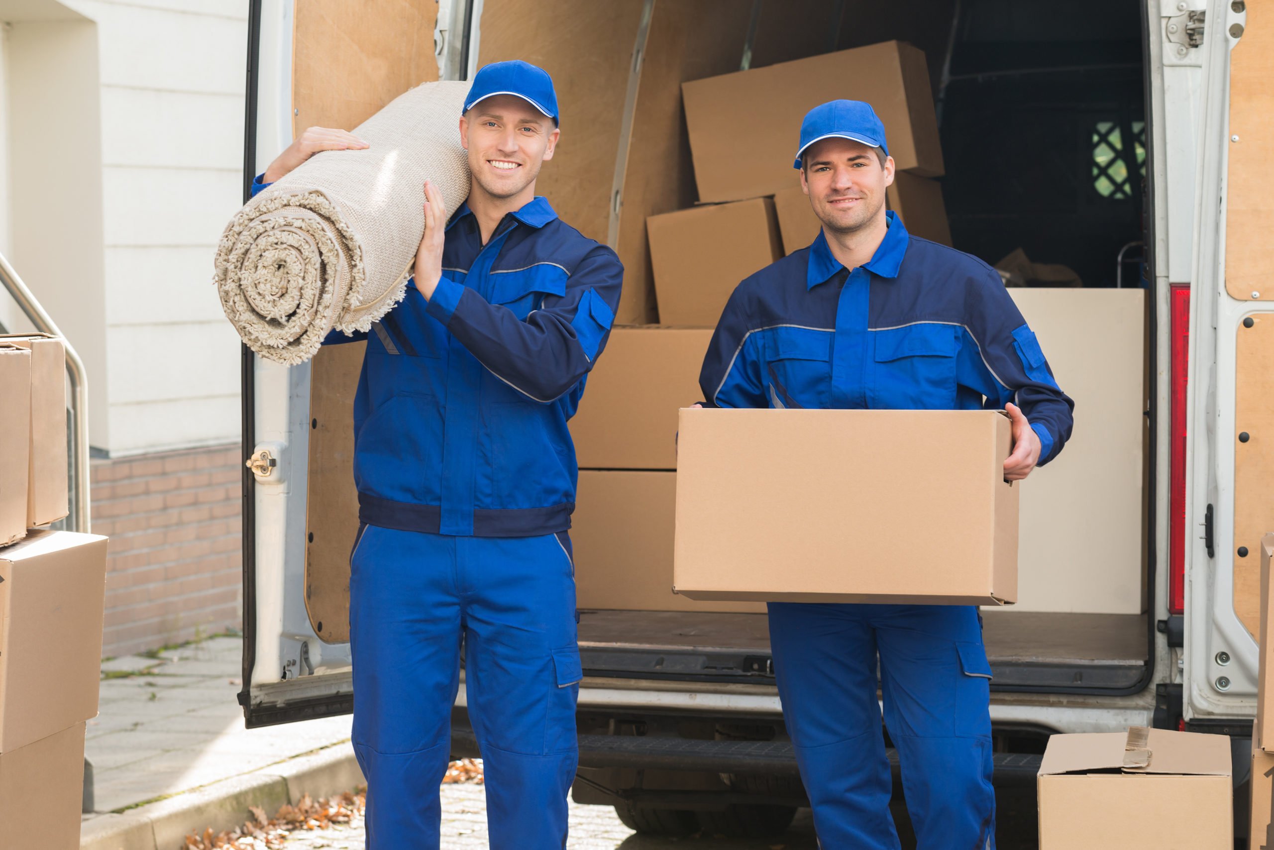 Portrait of happy delivery men carrying cardboard box and carpet outside van