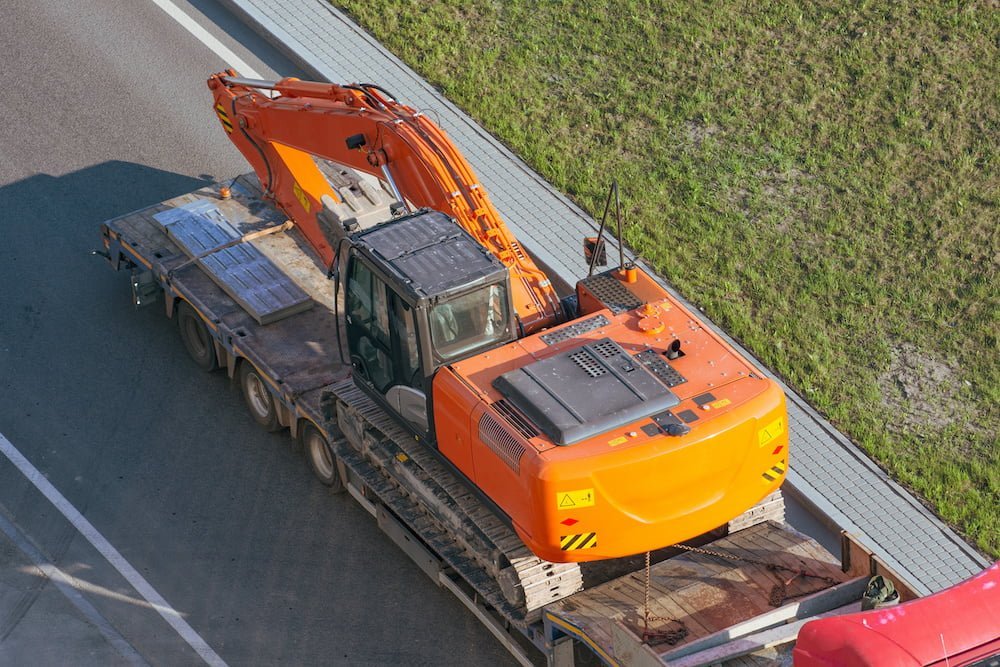 Truck with a long trailer platform for transporting heavy machinery, loaded excavator. Highway transportation