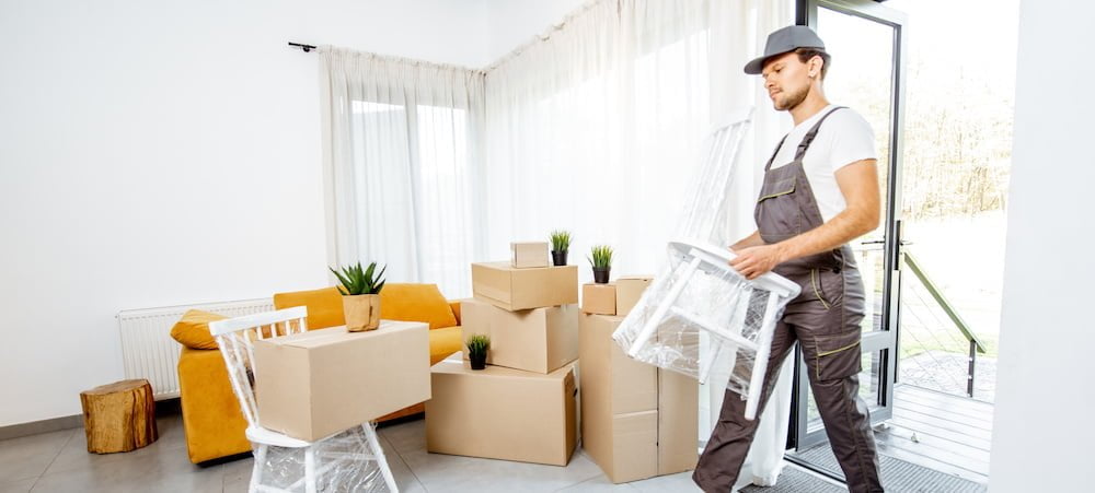 Handsome mover in workwear performing professional delivery of a goods and furniture during relocation process to a new house, interior view
