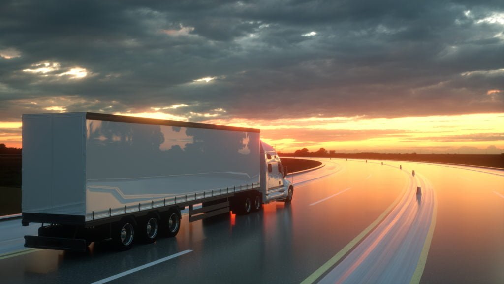 A semi trailer drives on an empty highway at sunset.