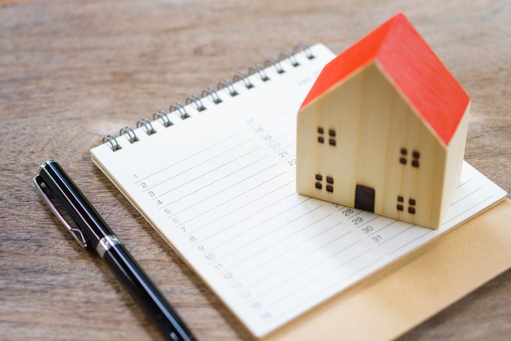 A miniature house model placed on top of a notebook sitting next to a pen
