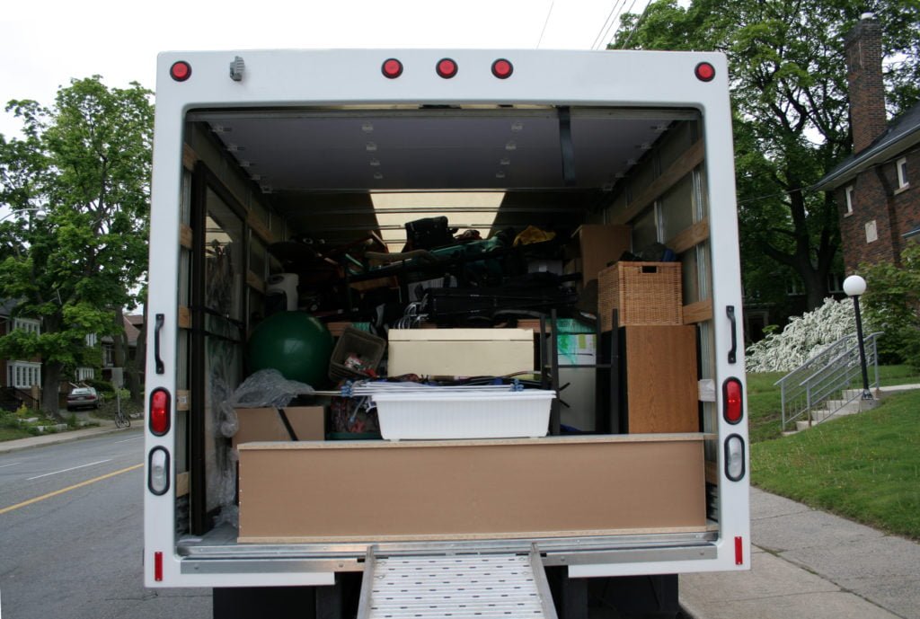 The back of an open moving truck reveals stacked boxes and furniture inside