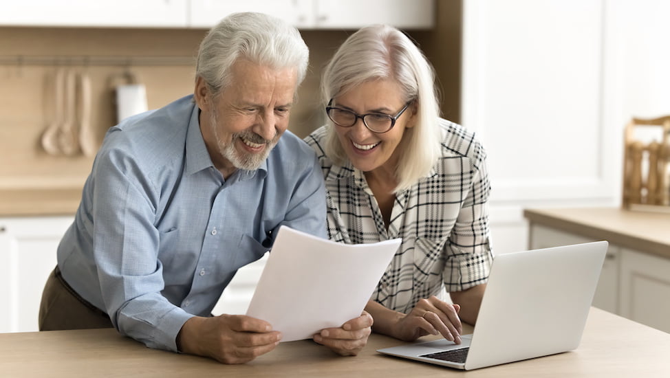 senior couple looking at paperwork in front of computer